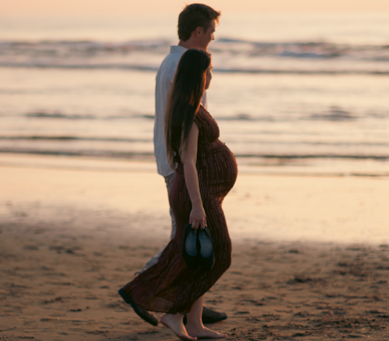 Pregnant woman and partner walking on the beach at sunset. Taken by The Hague birth photographer