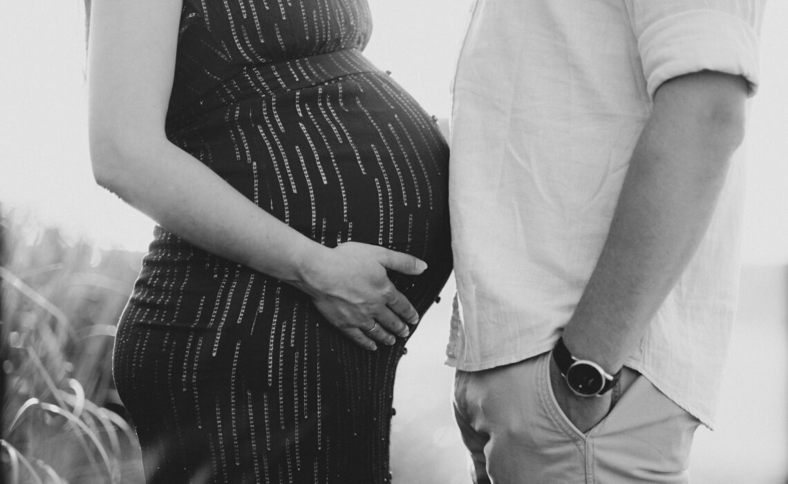 Black and white close up photo of pregnant wife and husband with bellies facing each other.