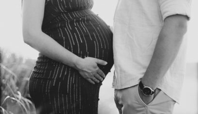 Black and white close up photo of pregnant wife and husband with bellies facing each other.