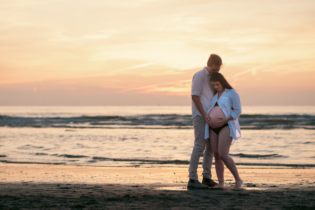 Pregnant couple on the beach during sunset.